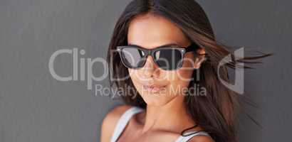 Beautiful, attractive and trendy portrait of a young woman isolated against a grey wall. Stylish, sexy and funky girl wearing sunglasses against a copy space background with a cool facial attitude