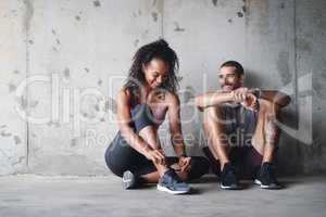 Get up and get going. Full length shot of a sporty young couple sitting down and resting against a wall.