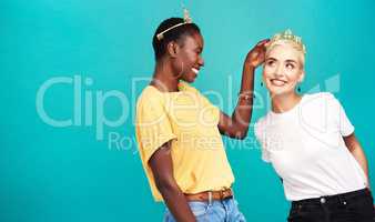 Every woman is a queen. Studio shot of a young woman putting a crown on her friend against a turquoise background.