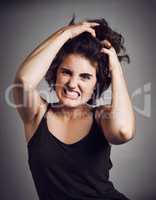 Cant contain the rage. Studio portrait of an attractive young woman pulling her hair with rage while standing against a grey background.