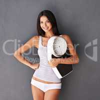 Slim, fit and healthy woman holding a scale against grey copy space background. Portrait of a beautiful female showing weight loss and benefits of a healthy lifestyle and balanced diet