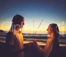 In your light, Ive learnt how to love. a young couple playing with sparklers on the beach at night.