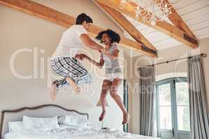 Were taking a leap of faith together. Full length sho of a playful young couple jumping on bed together at home.