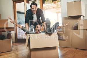 Homeowners moving in, having fun, feeling carefree and excited while playing, joking and laughing. Young interracial couple relocating or buying a new property and sitting in a cardboard box at home