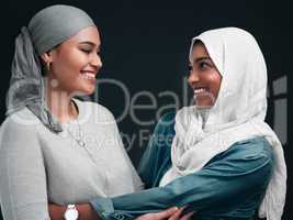 I am so grateful to have you as my friend. two attractive young women wearing hijabs and embracing each other against a black background in the studio.