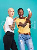 Lucky to have a best friend like her. Studio shot of two young women taking selfies together against a turquoise background.