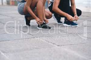 Theres no chance to trip this up. Closeup shot of two unrecognisable people tying their laces while exercising outdoors.