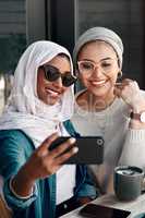 Were definitely uploading this. Cropped shot two affectionate young girlfriends taking a selfie together at a cafe while dressed in hijab.