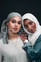 Protecting each other, always. two attractive young women wearing hijabs and standing close together against a black background in the studio.