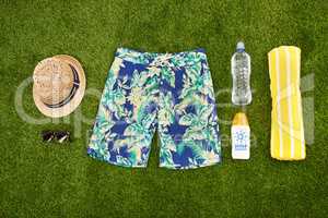 Mens casual summer fashion with accessories items, overhead top view. Marketing or advertising beach or pool swim clothes and equipment for men on fresh cut grass or astro turf over copy space.