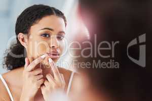 Squeezing might leave you with permanent marks. a beautiful young woman squeezing a pimple in the mirror.