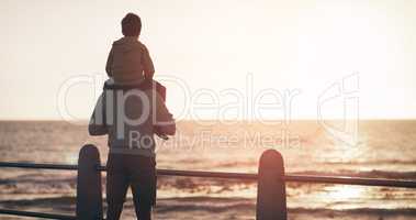 Such a sight will always remain beautiful. Rearview shot of a father carrying his son on his shoulders while watching the sun set at the beach.