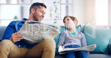 Making sure he knows that knowledge is power. a handsome father and son reading the newspaper together while sitting on a couch at home.