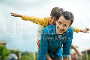 Taking flight with my little man. Portrait of a cheerful young father giving his son a piggyback ride outdoors.