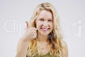 I definitely approve. Studio portrait of an attractive young woman giving a thumbs up against a grey background.