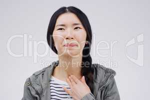 My throat feels so scratchy today. Studio shot of a young woman suffering with a sore throat against a grey background.