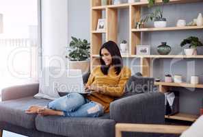 Time for some weekend blogging. an attractive young woman using her laptop while relaxing on a sofa at home.