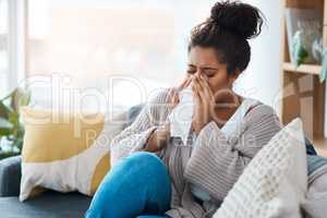 Its that awful season again. a young woman blowing her nose with a tissue at home.