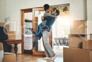 Joyful interracial couple moving in to a new home together hugging feeling happy and excited. Diverse, loving and young lovers relocating to a house and celebrating by embracing