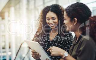 Our work will be so much easier with this tool. two attractive businesswomen using a digital tablet together while standing in a modern workplace.