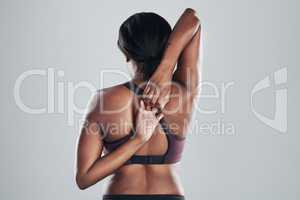 Nothing is a stretch too far. Rearview shot of an athletic young woman stretching her arms against a grey background.