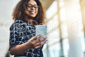 Find the right app to power your productivity. Low angle shot of an unrecognizable businesswoman using a smartphone while standing in a modern office.