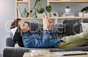 Lay back, chill and stay current. a handsome young man using a smartphone while lying on a couch at home.