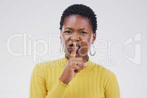 Keep quiet. Portrait of an attractive young woman posing with her finger on her lips against a grey background.