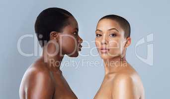 I see right into your soul. Portrait of two beautiful young women standing close to each other against a grey background.