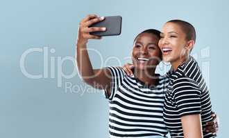 We have to show everybody. Studio shot of two beautiful young women taking a selfie together against a grey background.