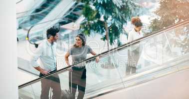 On the way to take a chance at success. two young businesspeople having a chat while going up an escalator in a modern workplace.