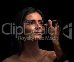 Brining out the best for that special occasion. Studio shot of an attractive young woman having makeup applied on her face against a dark background.