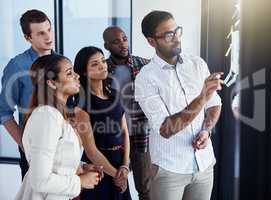 Hes got everyones attention with his new idea. a young businessman giving a demonstration on a glass wall to his colleagues in a modern office.