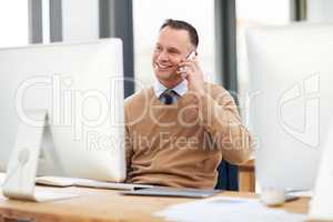Everything is turning out successful. a handsome middle aged businessman taking a phonecall while working on a computer in a modern office.
