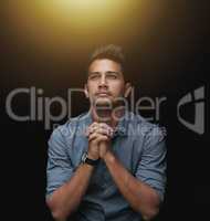 Asking for divine intervention. a handsome young businessman sitting with his hands together against a black background.