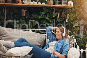 Before life runs away from you, relax. a young woman using headphones with her smartphone while relaxing in the garden at home.