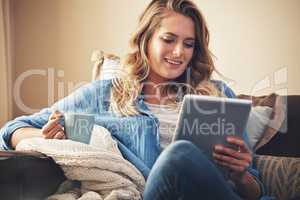 Wireless entertainment all weekend long. a relaxed young woman having coffee and using a digital tablet on the sofa at home.