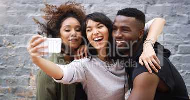 Its selfie time guys, strike a pose. a group of friends taking a selfie together while posing outdoors against a grey brick wall.