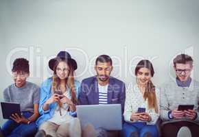 Making smart business choices using smart connections. Studio shot of a group of young businesspeople using wireless technology while sitting in line against a grey background.