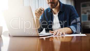 Time to handle some paperwork. a handsome young businessman sitting down and using his laptop while working from home.