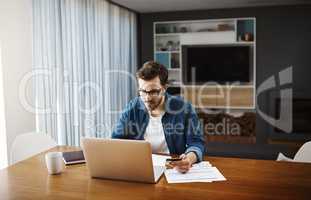 Time to have a look at whats on special online. a handsome young businessman sitting down and using his laptop to do some online shopping while working from home.