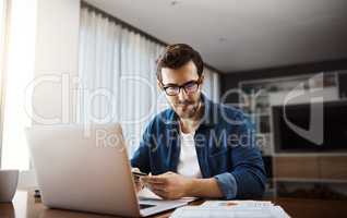 Hes doing some financial planning for his business. a handsome young businessman sitting down and using his laptop to do some online shopping while working from home.