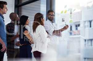 Everyone is finally on the same page. a young businessman giving a demonstration on a glass wall to his colleagues in a modern office.