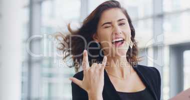 Im a rockstar in the business world. a young businesswoman showing a shaka hand sign while walking through a modern office.