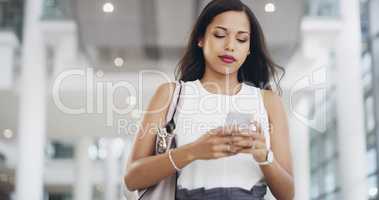 Shes got connections to contact. a young businesswoman using a smartphone while walking through a modern office.