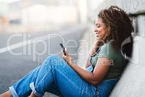 Im in my element, dont disturb. an attractive young woman sitting down and listening to music on her cellphone in the city.