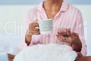 Keeping you connected from the start till finish. an unrecognizable woman drinking coffee and using her cellphone in bed at home.