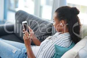 Searching for some new shows to stream on her cellphone. a young woman wearing earphones while using a cellphone at home.