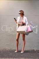 Young, trendy and fashionable female shopping alone, holding bags and on the phone. Rich caucasian woman with good style texting while standing in the street after buying sales items at retail stores