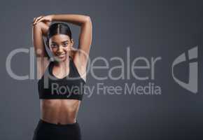 Its vital to first warm up your muscles. Studio portrait of a sporty young woman stretching her arms against a grey background.